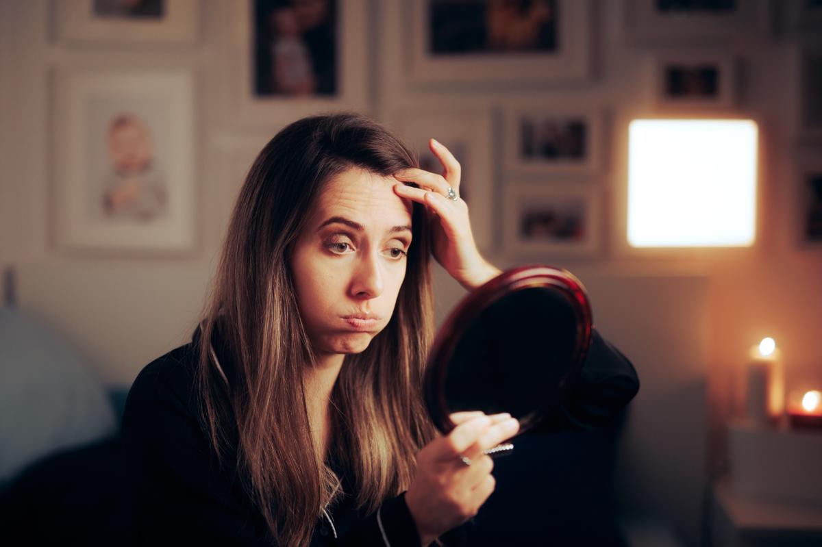 A woman looking for fine lines and wrinkles in a mirror.