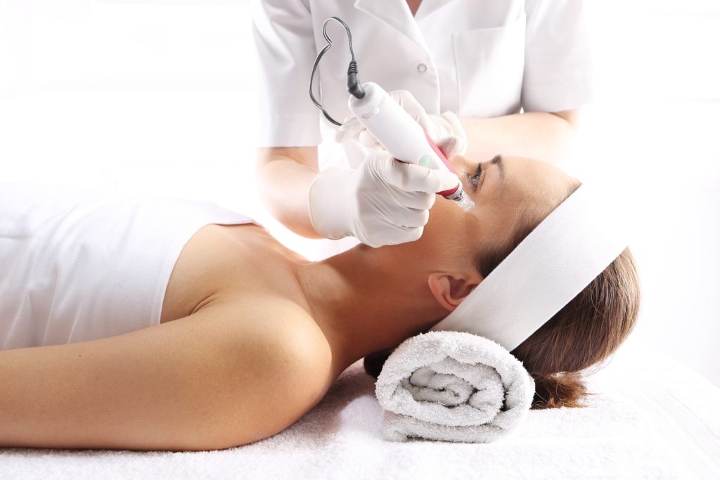 Beautician performs a microneedling treatment on a woman's face