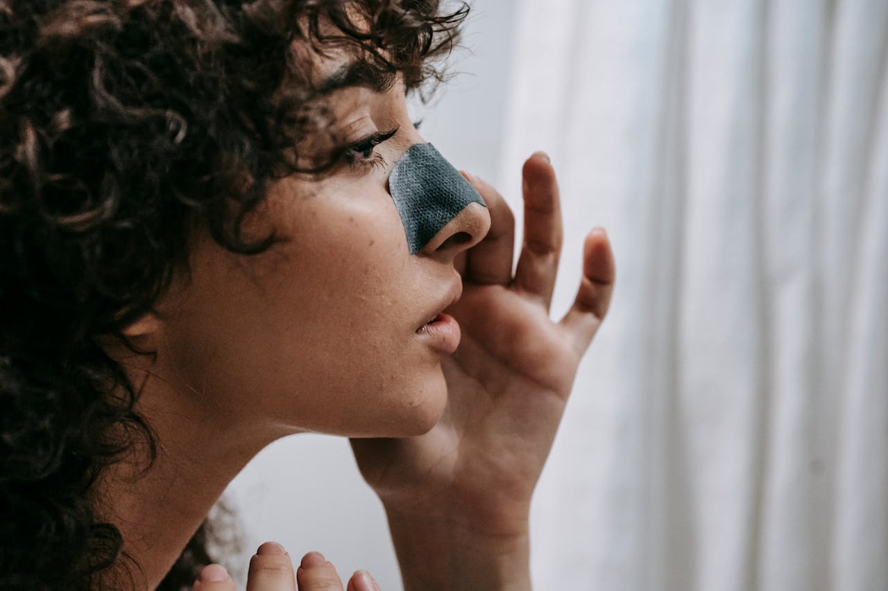 A woman with enlarged pores applying tape to her nose. 
