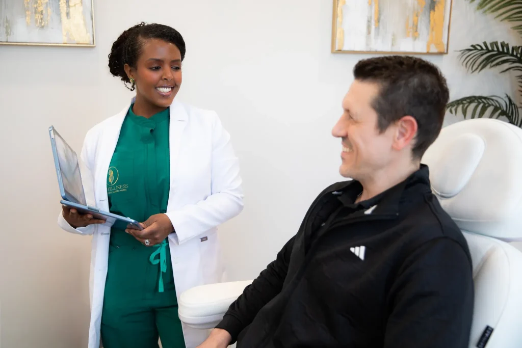 Provider at RxWellness Aesthetics & Anti-Aging reviews treatment details on a laptop with a patient in a clinic setting.